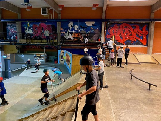 Barn med kickbikes i skatepark med graffititavlor i bakgrunden