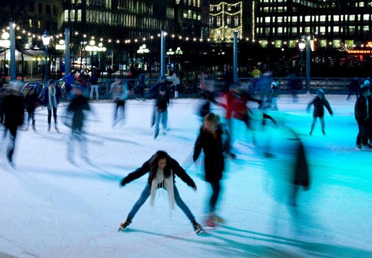 Ungdomar som åker skridskor på isbana kvällstid med höghus i Stockholms city i bakgrunden.